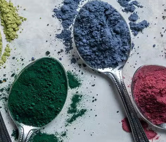 Three spoons filled with different colored powders on a white surface